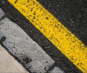 Ligne jaune vif sur la chaussée, en gros plan, le long d'un trottoir pavé
