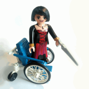 Femme fatale playmobil, debout sur un fauteuil roulant, une scie à la main, sourire carnassier
