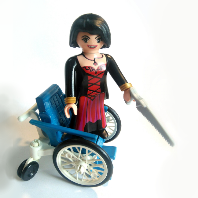 Femme fatale playmobil, debout sur un fauteuil roulant, une scie à la main, sourire carnassier